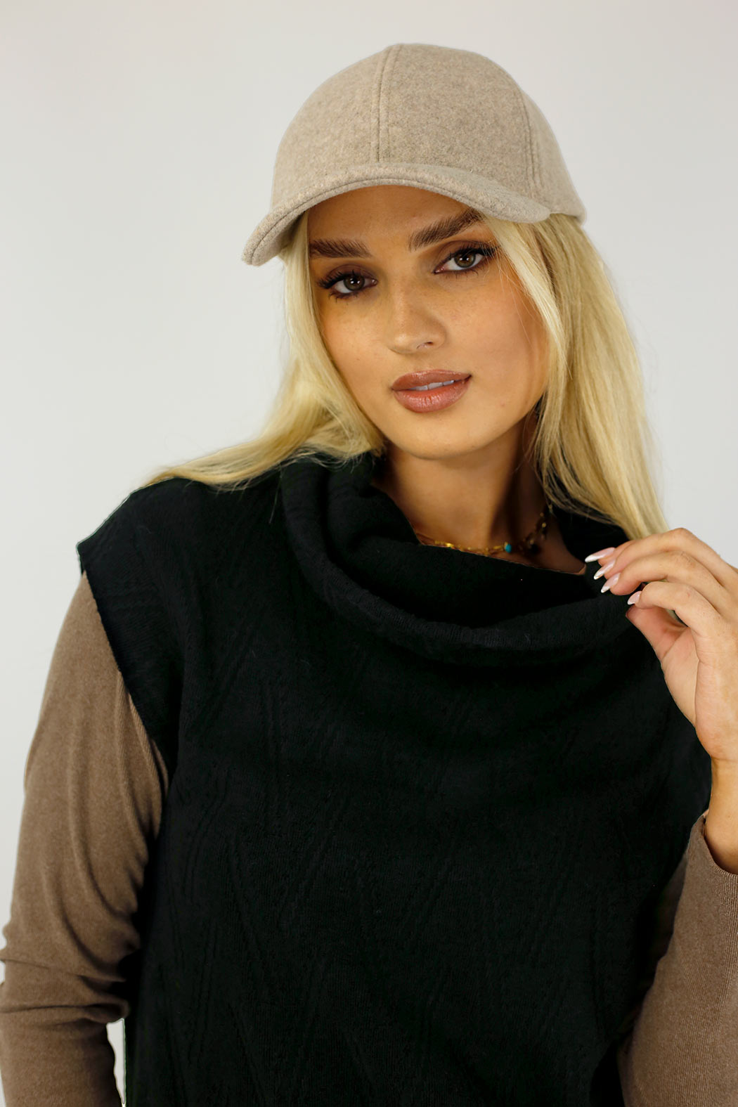 Black Cosy Cowl Vest layered over a tan skivvy, styled with a beige cap — elevated chevron knit and relaxed cowl neckline.
