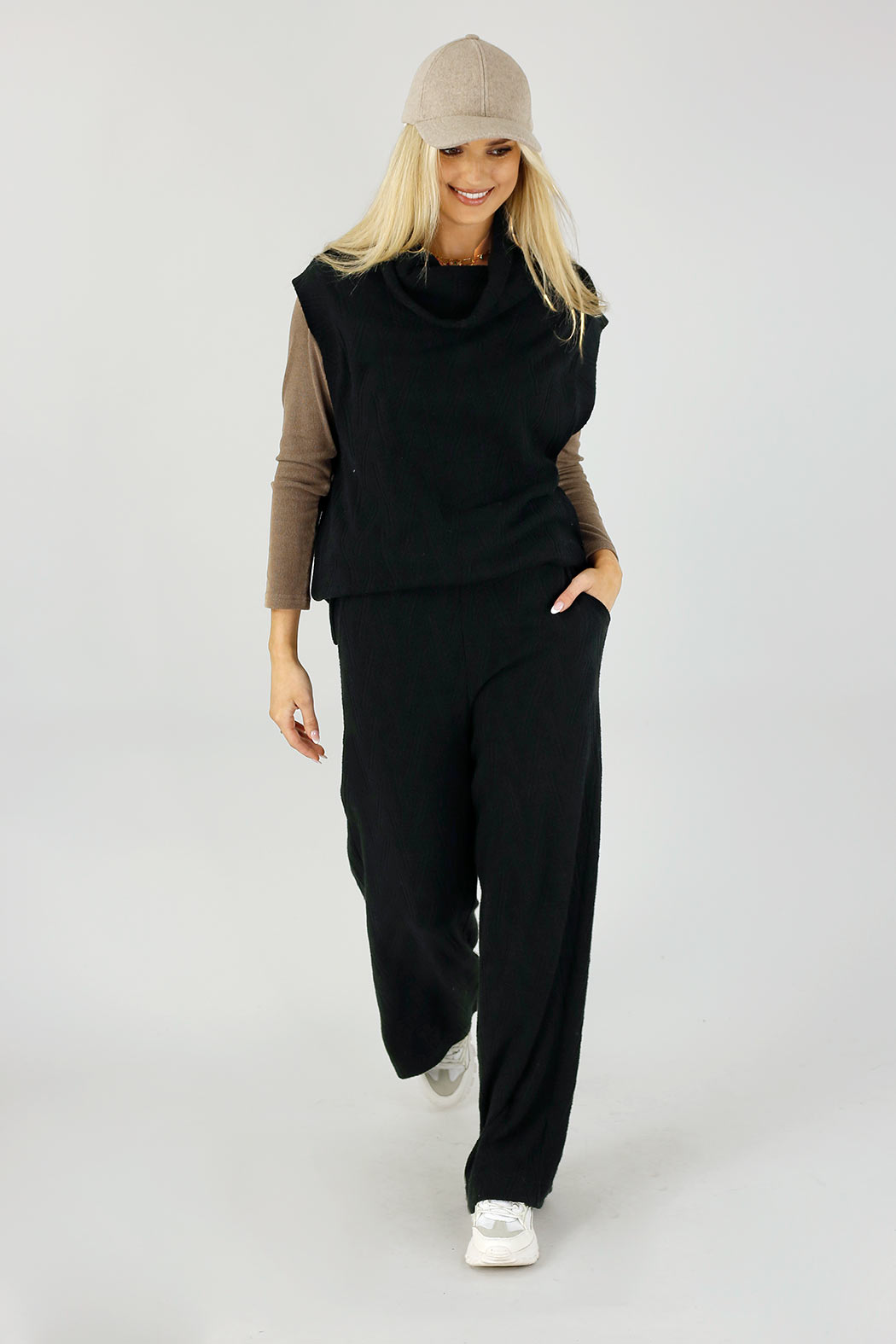 Black Cosy Cowl Vest layered over a taupe top, styled with relaxed trousers and a cap for an effortless, elevated look.