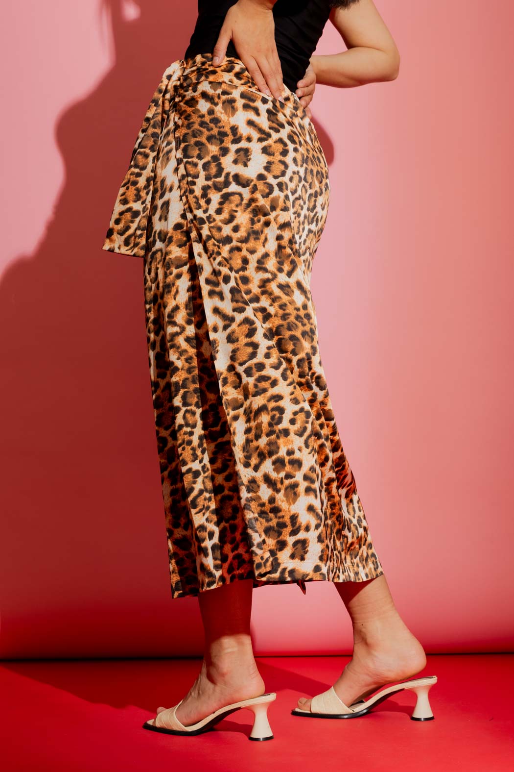 Effortless animal print knot front skirt in a flowing midi silhouette, styled with cream mules on a bold pink backdrop.