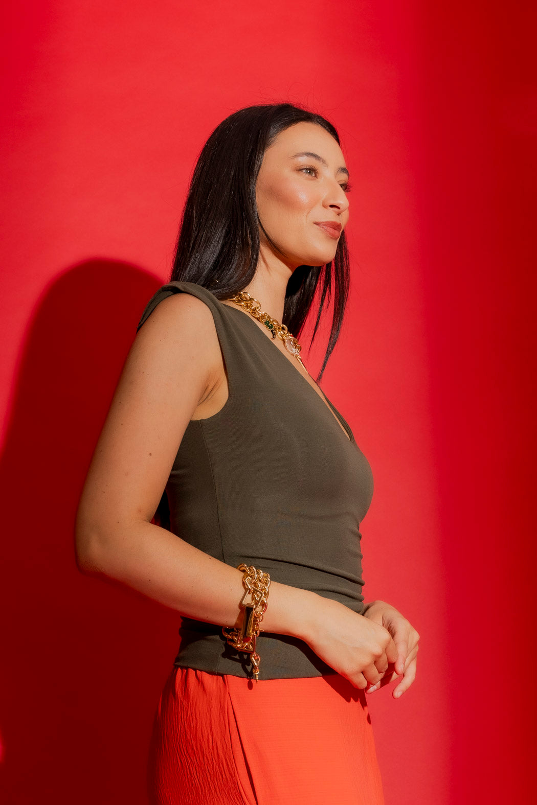 Forest Tencel Lust Cami in deep green, shown in profile with a V-neck and gold chain styling against a bold red backdrop.