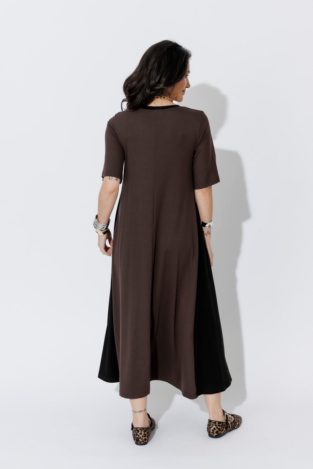 Chocolate Tencel Bella Dress in a fluid A-line, shown from behind with a layered black hem and leopard-print flats.