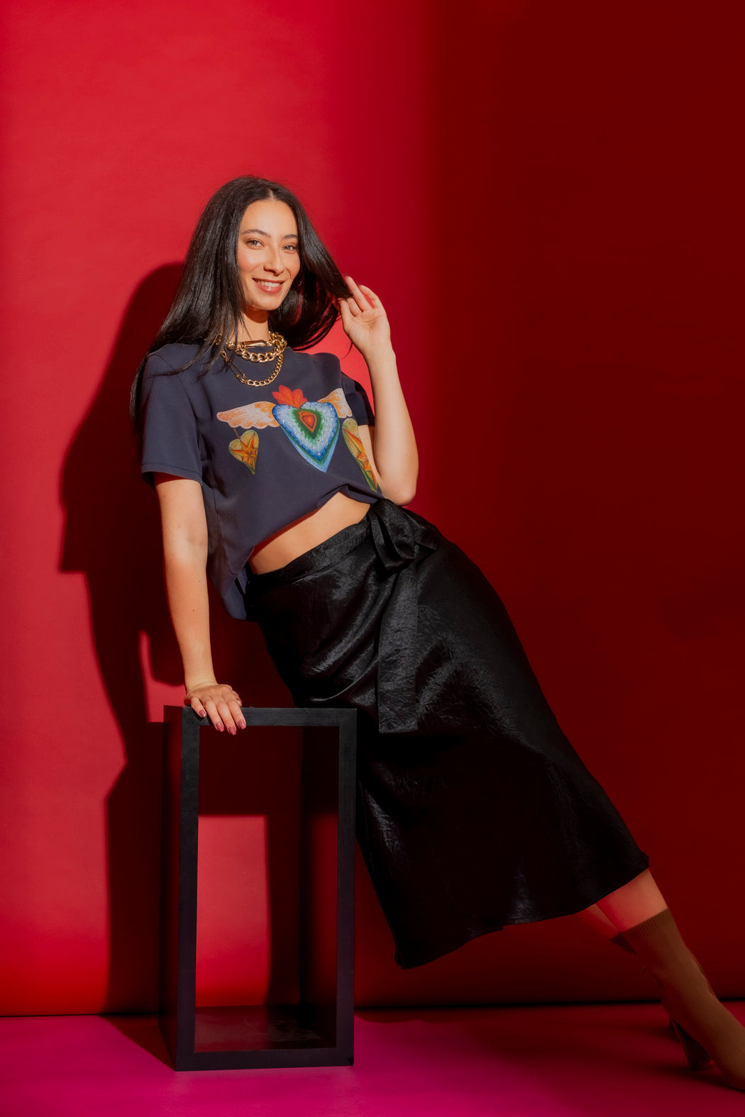 Black Bias Belted Skirt in lustrous satin, styled with a graphic tee against a bold red backdrop for an elevated look.