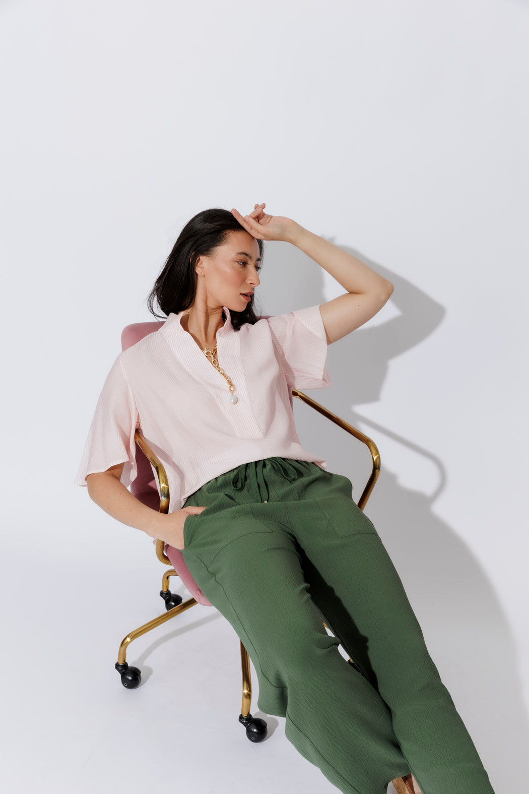 Pink Pinstripe Fluted Blogger Shirt styled with olive trousers, seated pose revealing stand collar and fluted sleeves.