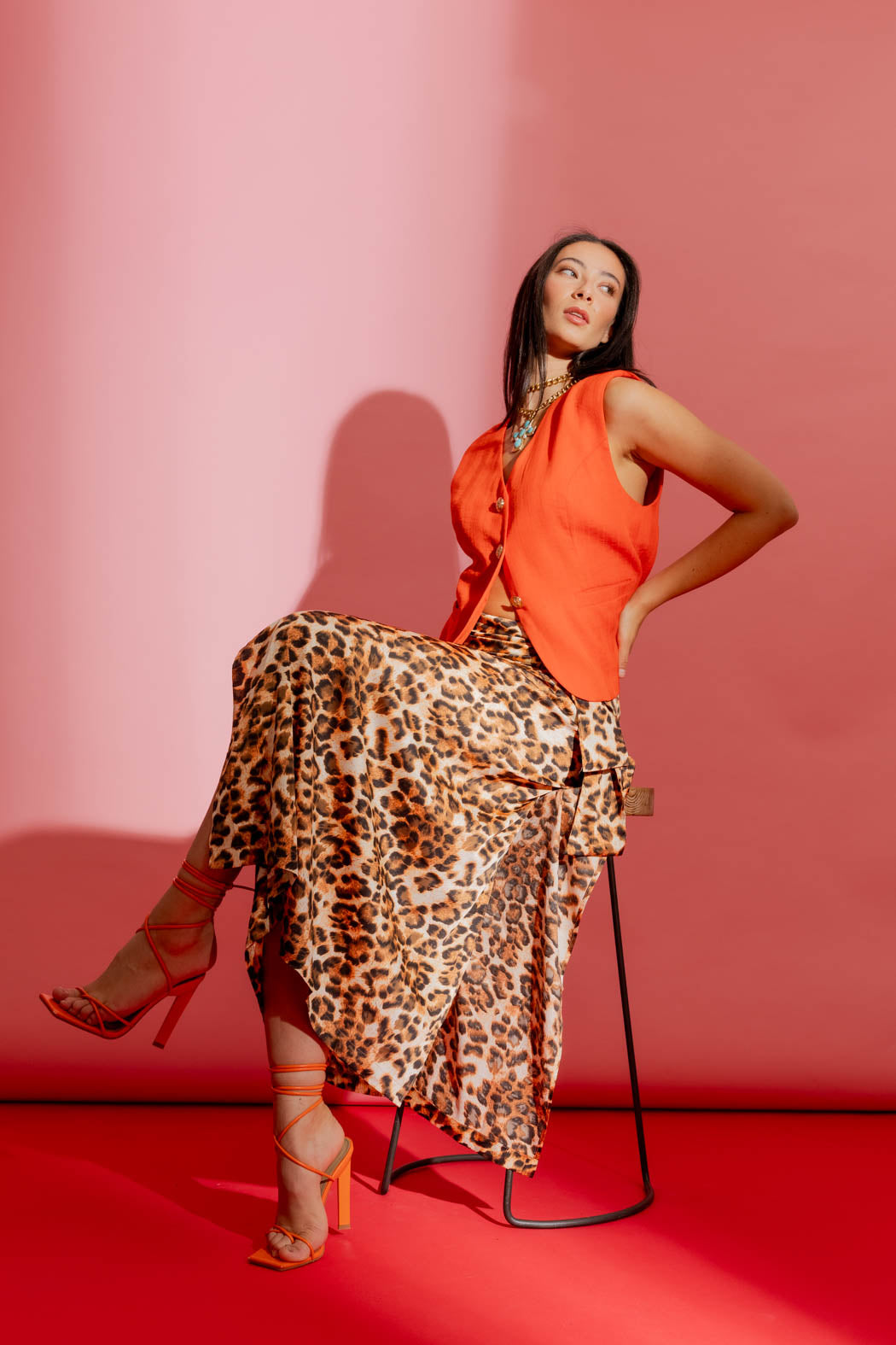 Animal print knot front skirt, styled with an orange top and strappy heels in a seated editorial pose on a coral set.