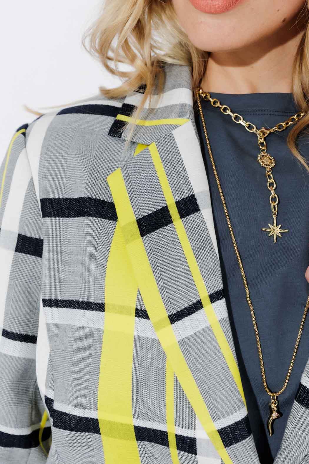 Close-up of the Neon Check Boyfriend Blazer's check lapel in grey, black and neon yellow, styled with a gold chain pendant.